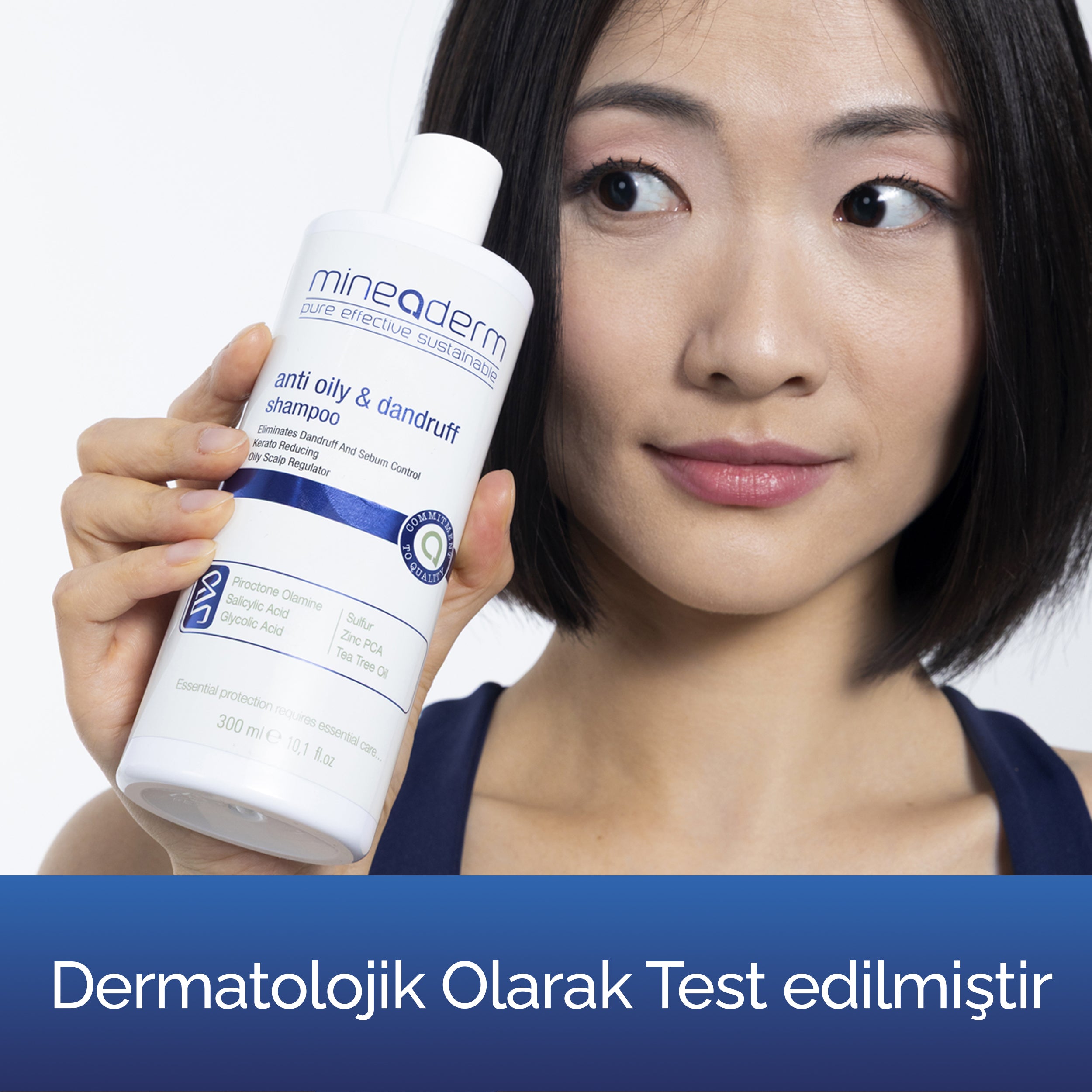 Gülümseyen bir kadın Mineaderm Anti Oily & Dandruff Shampoo şişesini tutuyor; dermatolojik olarak test edilmiş yağlı ve kepekli saçlar için bakım şampuanı.